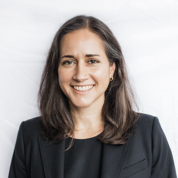 Zoila Hinson is a white woman in her early forties with brown hair and hazel eyes. She is wearing a black suit and is smiling.