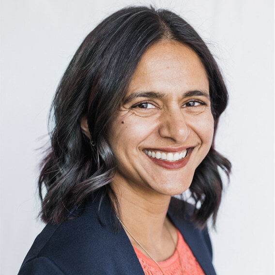 Tara Ramchandani is a South Asian woman in her 40s with shoulder length hair.  She is wearing a peach shell and blue blazer and is smiling.