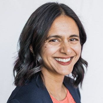 Tara Ramchandani is a South Asian woman in her 40s with shoulder length hair.  She is wearing a peach shell and blue blazer and is smiling.