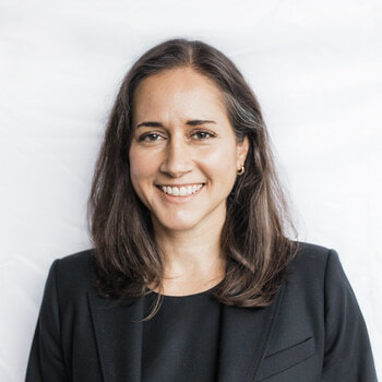 Zoila Hinson is a white woman in her early forties with brown hair and hazel eyes. She is wearing a black suit and is smiling.