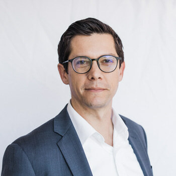 Stephen Hayes is a white man in his mid-40s with glasses. He is wearing a dark blue suit and white shirt.