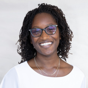 Sarah Ogundare is a Black woman in her early 20s with glasses. She is wearing a white top and is smiling.