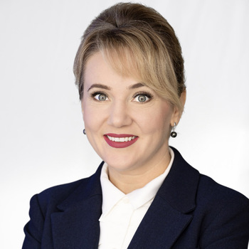 Lidia Shelley is a middle-aged white woman. She is wearing a blue jacket and a white shirt and is smiling. 