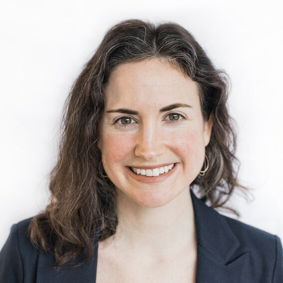 Brenna Kearns is a white woman in her 30s with brown hair. She is wearing a dark suit and metallic earrings and is smiling.